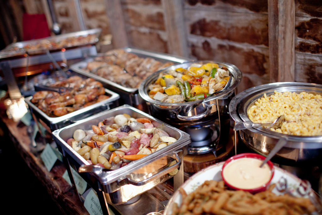 buffet table with mac and cheese, roasted chicken and vegetables, and assortment of potatoes