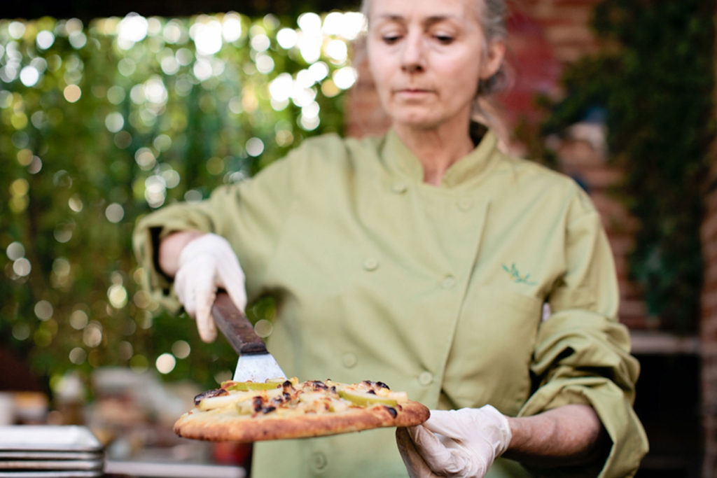 woman in green chef jacket serving wood fired pizza