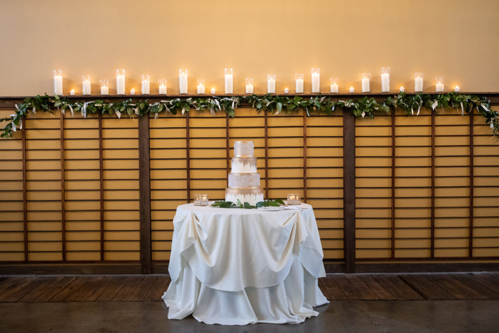 gold cake on white linen in front of wooden wall with candles